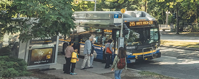 Passengers boarding a bus parked beneath the Expo Line near King George station on a sunny summer day