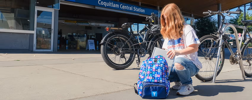 A transit user putting their laptop into their backpack in front of Coquitlam Central Station