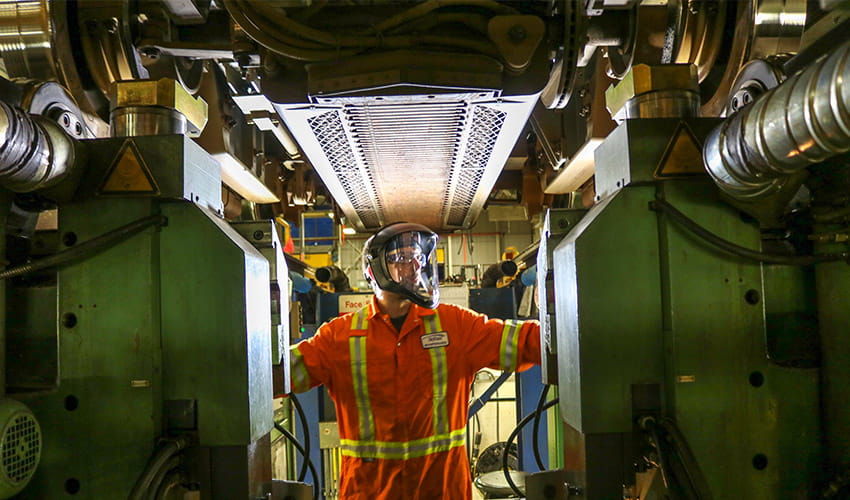 A worker in safety gear performs maintenance under a large piece of equipment at a bcrtc maintenance facility.