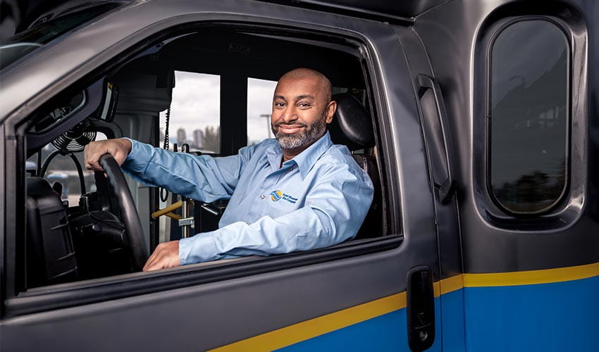 A smiling CMBC Community Shuttle Driver sitting confidently behind the wheel of a shuttle bus