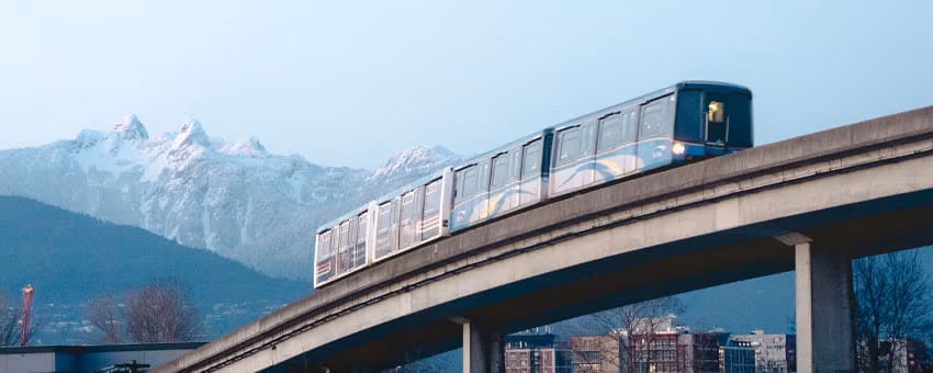 SkyTrain is on the overhead guideway. Snow capped mountains in the background.