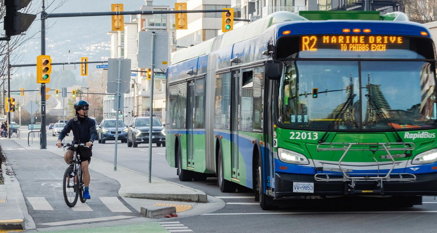 A cyclist stopped at a light in North Vancouver, with a RapidBus in the lane next to him.