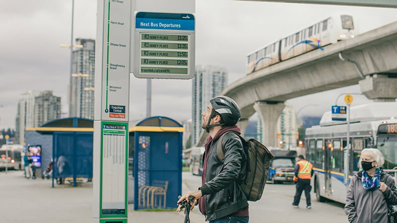 A cyclist looking up at a Next Bus display on the R3 RapidBus bus pole