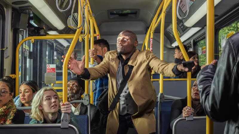 A man stands on a bus trying to grab the rails.