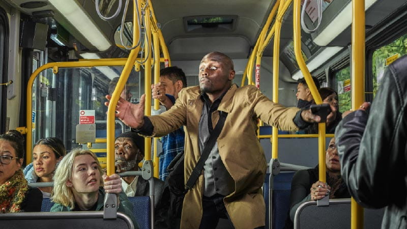 A man stands on a bus trying to grab the rails.