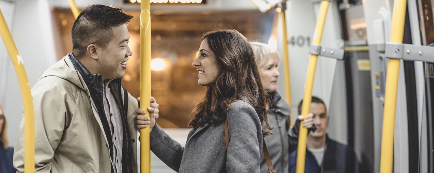 A diverse group of people riding the SkyTrain, with two individuals engaged in conversation and others seated or standing in the background