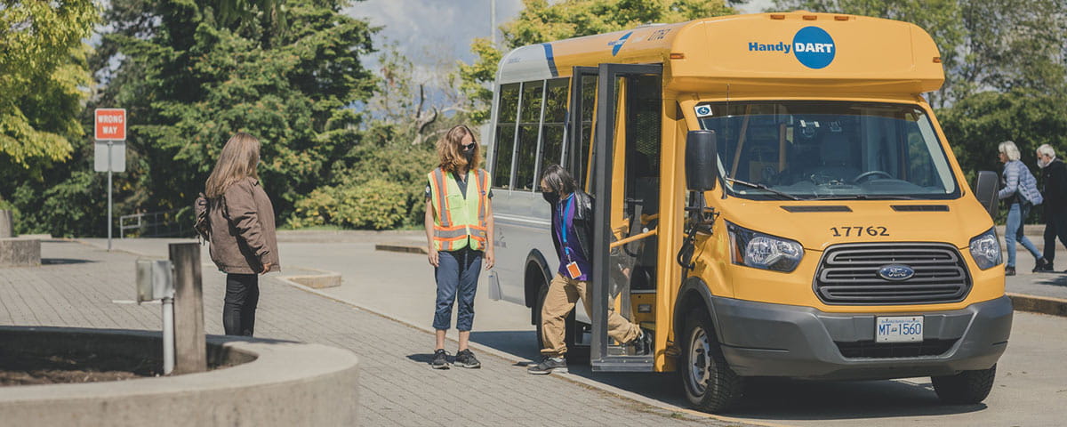 A man exiting a HandyDART vehicle while the driver is standing by for support.