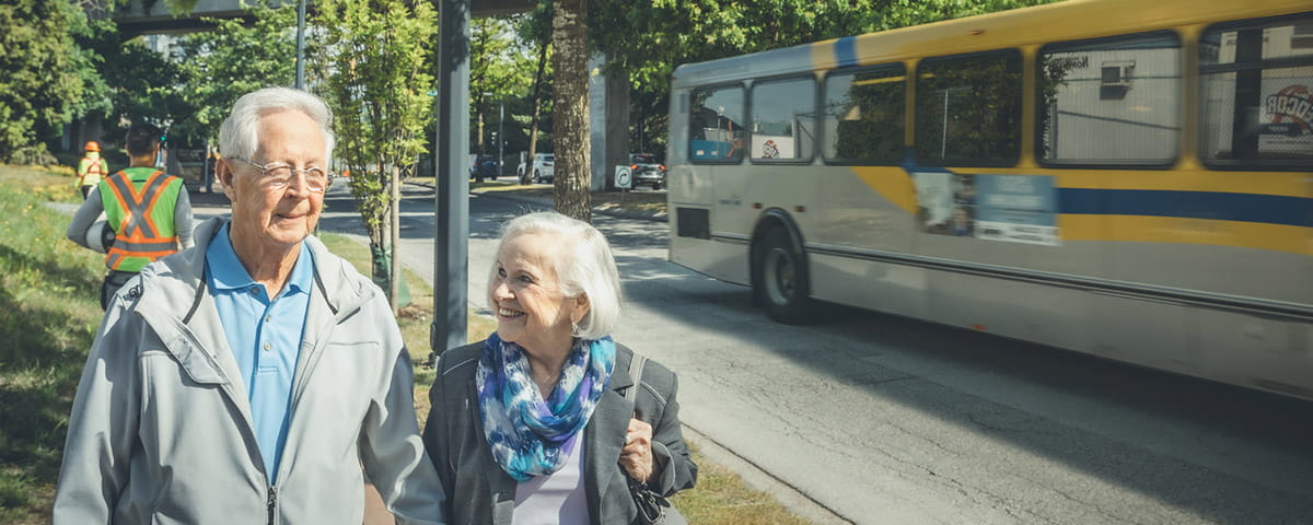 A senior couple enjoys their commute on a sunny day as a TransLink bus zips past them.