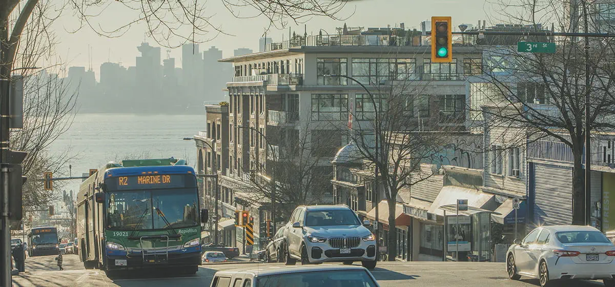 A RapidBus driving up a hill with a scenic view of downtown Vancouver in the background