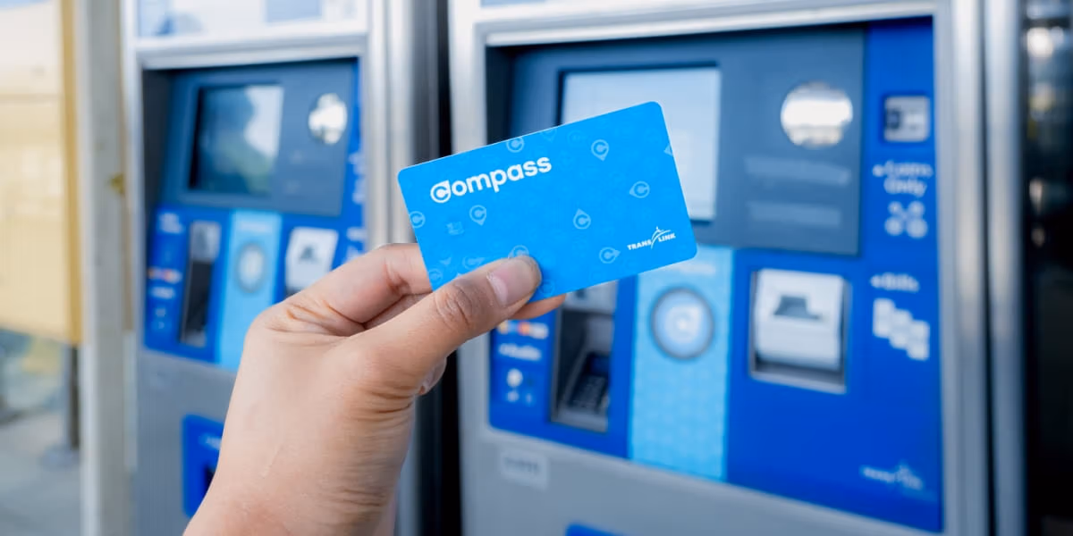 Image of a hand holding a compass card with a Compass Vending Machine in the background