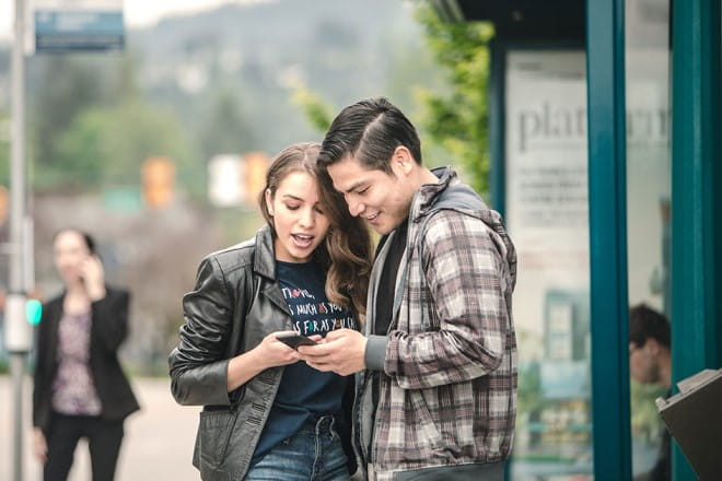 A man and woman looking at next bus times on a mobile phone outside a bus exchange