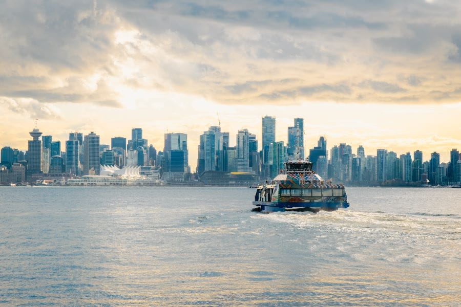 SeaBus sailing during cloudy sunset with downtown Vancouver skyline in background